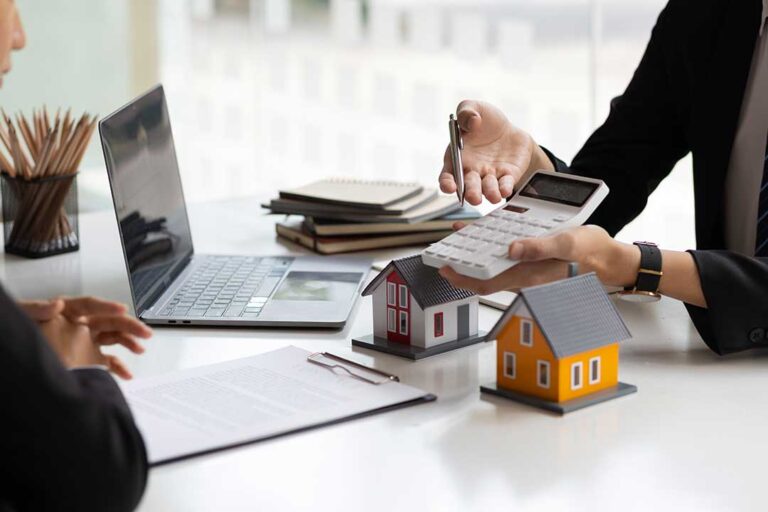 A family reviewing home documents at a dining table with a laptop, paperwork, and coffee mugs.